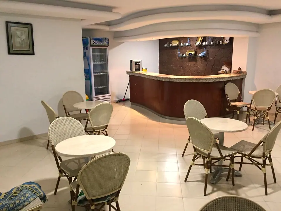 Cafétéria : tables rondes, chaises en rotin et comptoir en bois