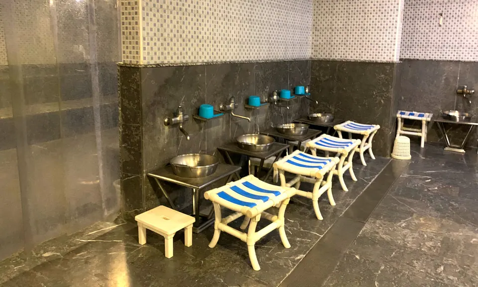 Salle de lavage du hammam : tabourets rayés bleu et blanc, bassines en inox et bols turquoise, murs en marbre gris